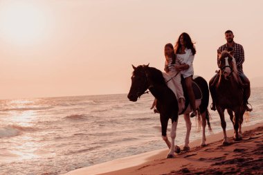 The family spends time with their children while riding horses together on a sandy beach. Selective focus. High quality photo