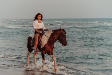 Yaz kıyafetleri içinde bir kadın gün batımında kumlu güzel bir sahilde ata binmekten hoşlanır. Seçici odaklanma. Yüksek kalite fotoğraf