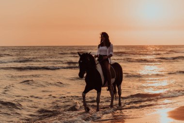Yaz kıyafetleri içinde bir kadın gün batımında kumlu güzel bir sahilde ata binmekten hoşlanır. Seçici odaklanma. Yüksek kalite fotoğraf