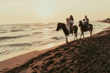 The family spends time with their children while riding horses together on a sandy beach. Selective focus. High quality photo
