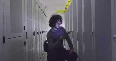 Modern bir sanal veri merkezi süperbilgisayarının sunucu odasında tablet bilgisayar üzerinde çalışan bilişim mühendisi ya da veri bilimci. Hippi gündelik kıyafetler giyer ve bir sandalyeye oturur.. 