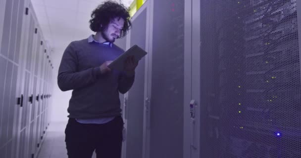 Itエンジニアやデータサイエンスの専門家は 現代のクラウドコンピューティング仮想データセンタースーパーコンピュータのサーバールームでタブレットコンピュータに取り組んでいます ラック廊下を歩くカジュアル服を身に着けているヒップスター — ストック動画