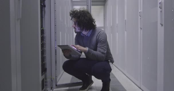Itエンジニアやデータサイエンスの専門家は 現代のクラウドコンピューティング仮想データセンタースーパーコンピュータのサーバールームでタブレットコンピュータに取り組んでいます ラック廊下で働くカジュアル服を身に着けているヒップスター — ストック動画