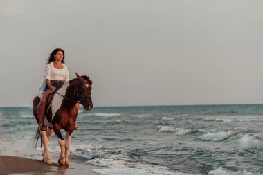 Yaz kıyafetleri içinde bir kadın gün batımında kumlu güzel bir sahilde ata binmekten hoşlanır. Seçici odaklanma. Yüksek kalite fotoğraf