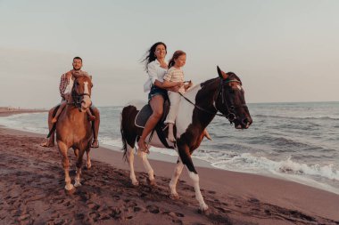 Aile kumlu bir sahilde birlikte ata binerken çocuklarıyla vakit geçirir. Seçici odaklanma. Yüksek kalite fotoğraf