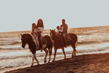The family spends time with their children while riding horses together on a sandy beach. Selective focus. High quality photo
