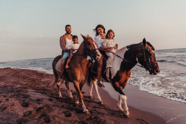 The family spends time with their children while riding horses together on a sandy beach. Selective focus. High quality photo