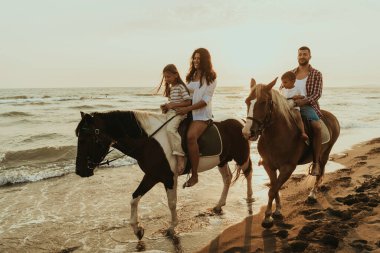 The family spends time with their children while riding horses together on a sandy beach. Selective focus. High quality photo