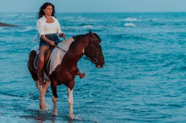 Yaz kıyafetleri içinde bir kadın gün batımında kumlu güzel bir sahilde ata binmekten hoşlanır. Seçici odaklanma. Yüksek kalite fotoğraf