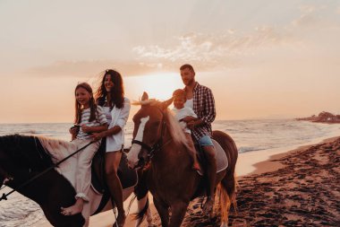 The family spends time with their children while riding horses together on a sandy beach. Selective focus. High quality photo