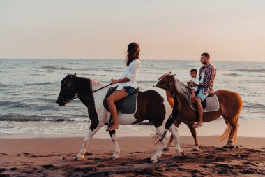 Aile kumlu bir sahilde birlikte ata binerken çocuklarıyla vakit geçirir. Seçici odaklanma. Yüksek kalite fotoğraf