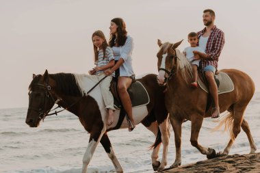 The family spends time with their children while riding horses together on a sandy beach. Selective focus. High quality photo