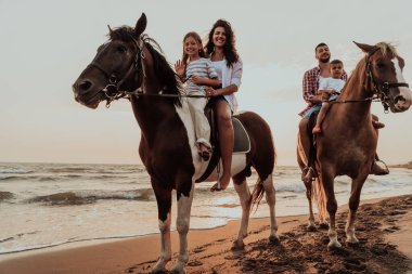 The family spends time with their children while riding horses together on a sandy beach. Selective focus. High quality photo