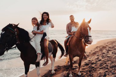 The family spends time with their children while riding horses together on a sandy beach. Selective focus. High quality photo