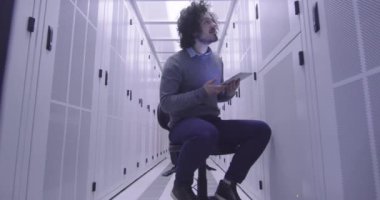 Modern bir sanal veri merkezi süperbilgisayarının sunucu odasında tablet bilgisayar üzerinde çalışan bilişim mühendisi ya da veri bilimci. Hippi gündelik kıyafetler giyer ve bir sandalyeye oturur.. 