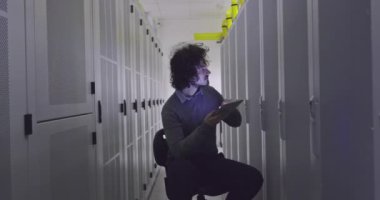 Modern bir sanal veri merkezi süperbilgisayarının sunucu odasında tablet bilgisayar üzerinde çalışan bilişim mühendisi ya da veri bilimci. Hippi gündelik kıyafetler giyer ve bir sandalyeye oturur.. 