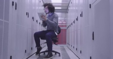 Modern bir sanal veri merkezi süperbilgisayarının sunucu odasında tablet bilgisayar üzerinde çalışan bilişim mühendisi ya da veri bilimci. Hippi gündelik kıyafetler giyer ve bir sandalyeye oturur.. 