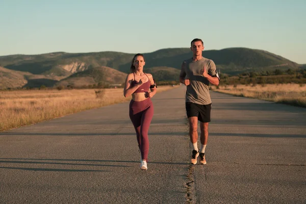 早朝街をジョギングする健康な若いカップル背景に美しい日の出と 高品質の写真 — ストック写真