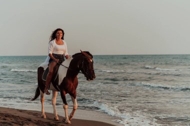 Yaz kıyafetleri içinde bir kadın gün batımında kumlu güzel bir sahilde ata binmekten hoşlanır. Seçici odaklanma. Yüksek kalite fotoğraf