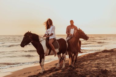A loving couple in summer clothes riding a horse on a sandy beach at sunset. Sea and sunset in the background. Selective focus. High quality photo