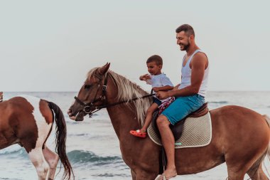 Baba ve oğul deniz kenarında at sürmekten hoşlanırlar. Seçici odaklanma. Yüksek kalite fotoğraf