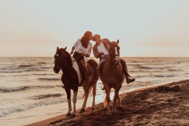 A loving couple in summer clothes riding a horse on a sandy beach at sunset. Sea and sunset in the background. Selective focus. High quality photo