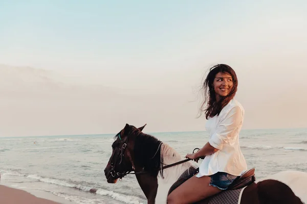 夏の服の女性は 日没時に美しい砂浜で馬に乗るのを楽しんでいます 選択的フォーカス 高品質の写真 — ストック写真