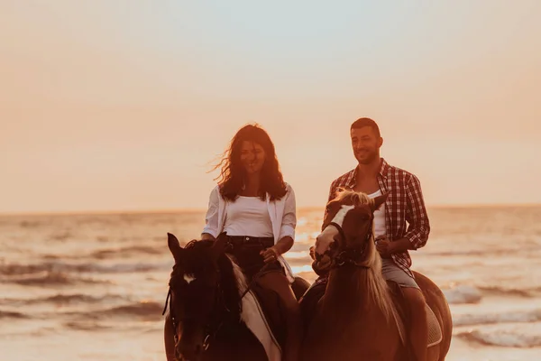 A loving couple in summer clothes riding a horse on a sandy beach at sunset. Sea and sunset in the background. Selective focus. High quality photo