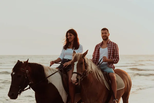 サンセットの砂浜で馬に乗って夏の服を愛するカップル 海と夕日を背景に 選択的フォーカス 高品質の写真 — ストック写真