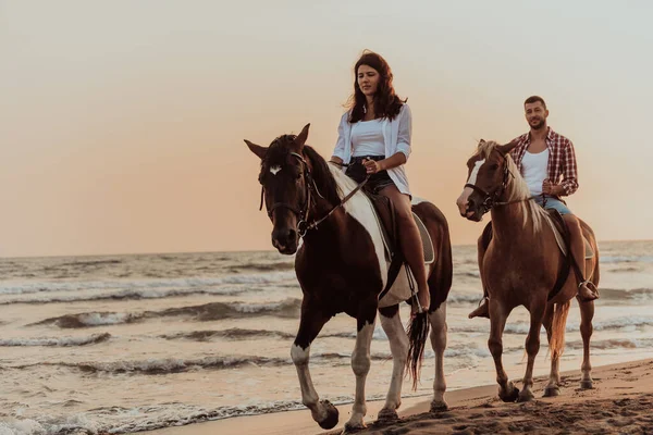 一对穿着夏装的恋人在日落时分骑马在沙滩上 背景是大海和日落 有选择的重点 高质量的照片 — 图库照片