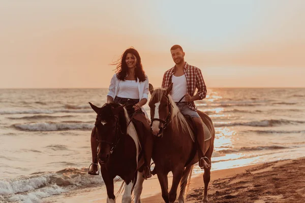 サンセットの砂浜で馬に乗って夏の服を愛するカップル 海と夕日を背景に 選択的フォーカス 高品質の写真 — ストック写真