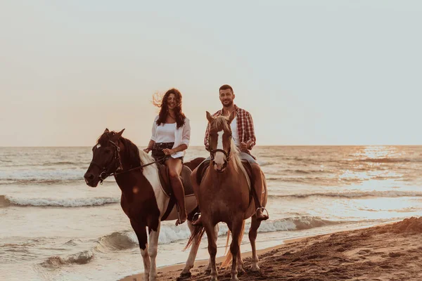 A loving couple in summer clothes riding a horse on a sandy beach at sunset. Sea and sunset in the background. Selective focus. High quality photo