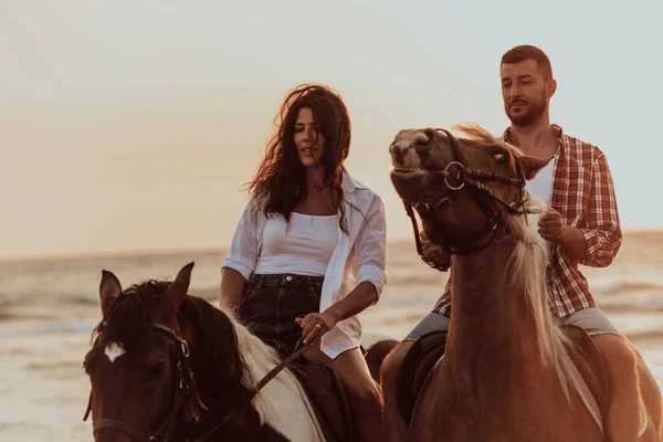 A loving couple in summer clothes riding a horse on a sandy beach at sunset. Sea and sunset in the background. Selective focus. High quality photo