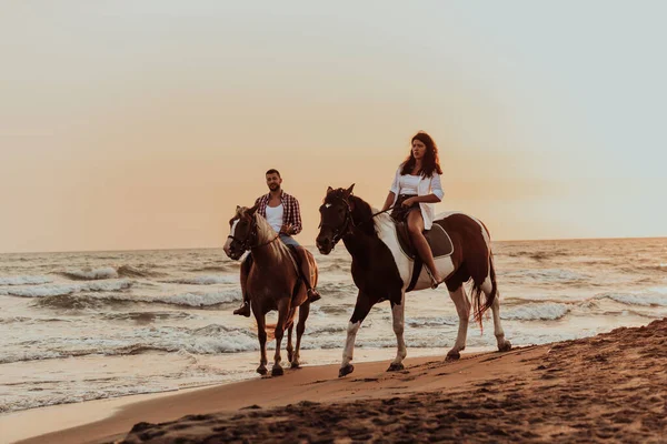 A loving couple in summer clothes riding a horse on a sandy beach at sunset. Sea and sunset in the background. Selective focus. High quality photo