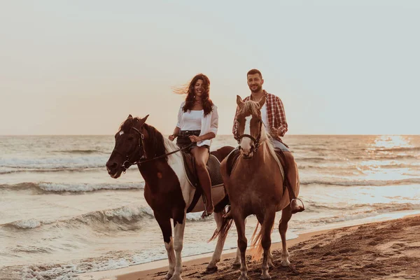 A loving couple in summer clothes riding a horse on a sandy beach at sunset. Sea and sunset in the background. Selective focus. High quality photo