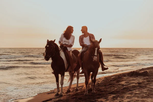 A loving couple in summer clothes riding a horse on a sandy beach at sunset. Sea and sunset in the background. Selective focus. High quality photo