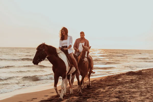 A loving couple in summer clothes riding a horse on a sandy beach at sunset. Sea and sunset in the background. Selective focus. High quality photo
