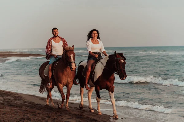 A loving couple in summer clothes riding a horse on a sandy beach at sunset. Sea and sunset in the background. Selective focus. High quality photo