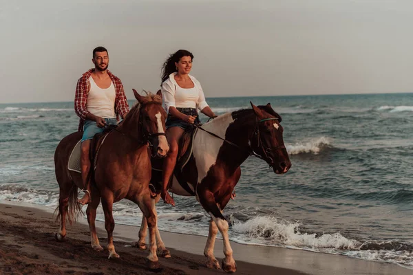 A loving couple in summer clothes riding a horse on a sandy beach at sunset. Sea and sunset in the background. Selective focus. High quality photo