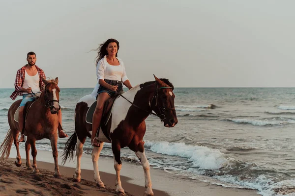 A loving couple in summer clothes riding a horse on a sandy beach at sunset. Sea and sunset in the background. Selective focus. High quality photo