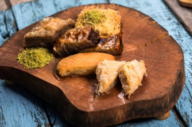 Ramazan Kareem, geleneksel Türk ortadoğu iftarı Baklava 'yı şam fıstıklı ve kır ağacından yapılmış ahşap tabakta taze bal ve klasik mavi arka plan masasıyla donatıyor. Üst Manzara. Yüksek kalite fotoğraf