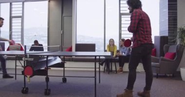 Günlük iş hayatına başlamak. İş adamları modern yaratıcı ofis alanında masa tenisi oynarken bir grup kadın iş arkadaşı proje üzerinde çalışıyor ve arka planda buluşuyorlar. Yüksek kalite