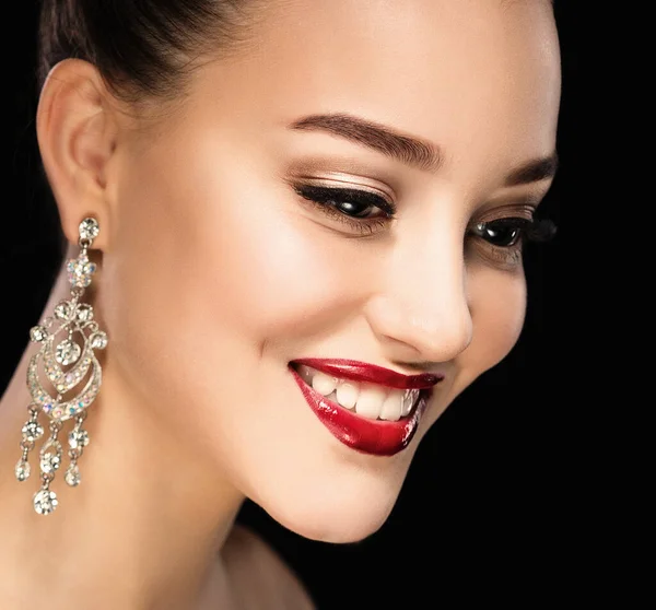 Vacker brunett kvinna med ljusa smink och smycken örhängen leende närbild. Röda läppar och naglar, kväll make-up, lyxigt utseende. — Stockfoto