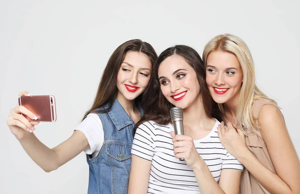 生活方式 友谊和人的观念 三位年轻女性带着话筒唱歌 用智能手机在白色背景下拍照 — 图库照片