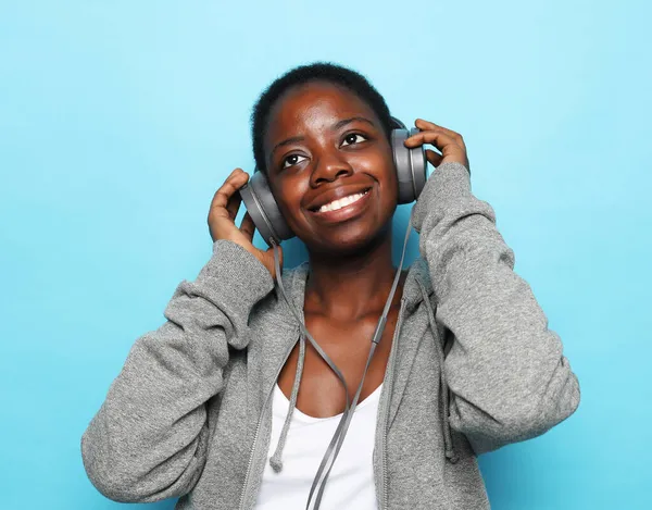 Όμορφη νεαρή Αφροαμερικανή γυναίκα να ακούσετε μουσική πάνω από το μπλε φόντο. — Φωτογραφία Αρχείου