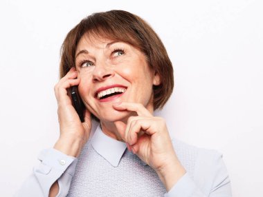 Modern yaşam tarzı, yaşlılar, iletişim ve elektronik aletler. Beyaz gri arka planda akıllı telefonlu mavi gömlek giyen yaşlı bir kadın..