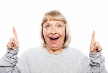 İyimser ifadeye sahip güzel yaşlı kadın modeli, bir şey tarafından heyecanlanıp, ön parmağını kaldırdığını, promosyon metnin için fotokopi aletiyle beyaz arkaplana karşı poz verdiğini gösteriyor.