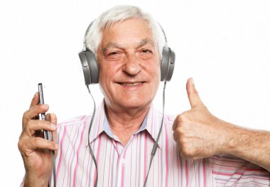 Gündelik kıyafetleri ve kulaklıkları olan yakışıklı yaşlı adam beyaz arka planda cep telefonu ve gülümseme kullanarak müzik dinliyor.