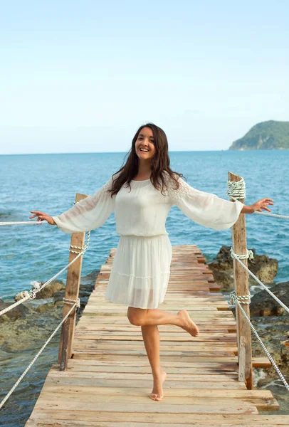 若い幸せなブルネットの女性が白いドレスを着て海の近くにポーズをとって 橋の上で 夏時間 ライフスタイルと旅行のコンセプト — ストック写真