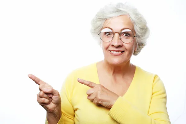 Smiling elderly woman lady 60s years old in yellow sweater pointing index fingers aside up on mock up copy space — Stock Photo, Image